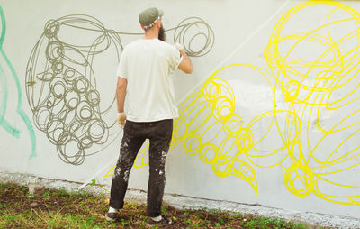Rear view full length of street artist painting graffiti on wall