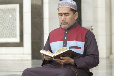 Mature man reading koran while sitting at mosque