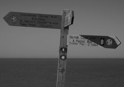 Information sign by sea against sky