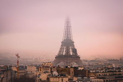 Communications tower in city against sky during sunset