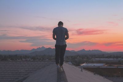 Rear view of man walking on rooftop against sky during sunset