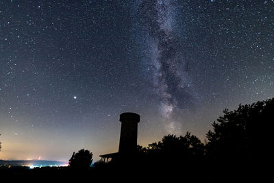 Low angle view of silhouette tower against sky with milkyway at night