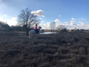 Girl riding horse on grass against sky