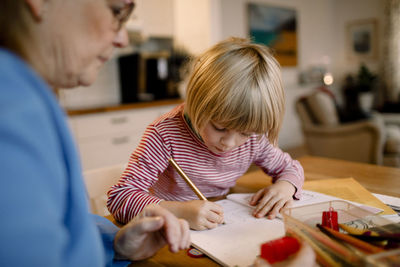 Boy doing homework by grandmother at table