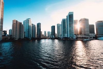 Modern buildings by sea against sky at sunset