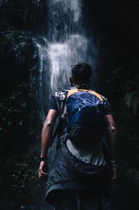 Rear view of man looking at waterfall in forest