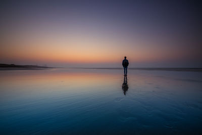 Silhouette man standing in sea against sky during sunset