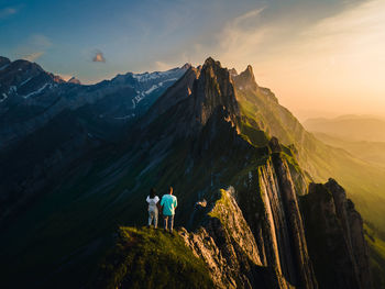 Rear view of men on mountain against sky during sunset