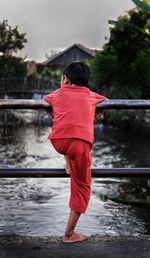 Rear view of boy standing by railing against river
