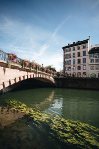 Bridge over river by buildings against sky