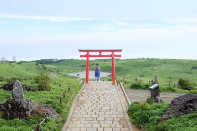 Rear view of man under japanese torii gate against sky