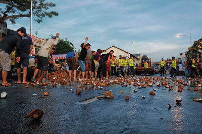People breaking coconuts on road in city against sky