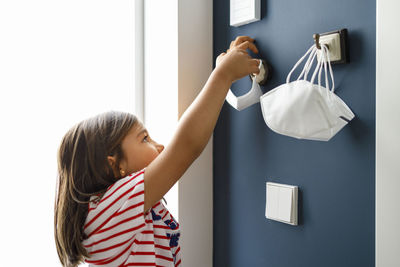 Girl removing protective face mask from hook at home during covid-19