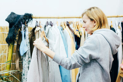 A woman is holding a shirt on a hanger in a clothing store and is about to try it on.