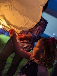 Young girl and woman lighting paper lantern 