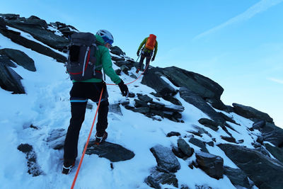 Low angle view of people hiking on snowcapped mountain against sky