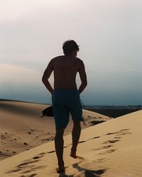 Rear view of shirtless man standing on sand at beach