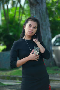 Portrait of woman standing against tree trunk