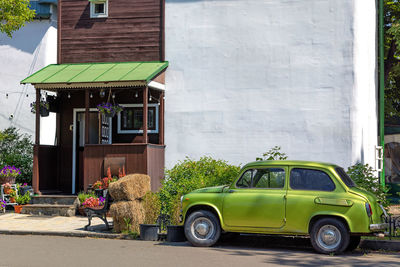 An old small car stands at the porch of a rural house.