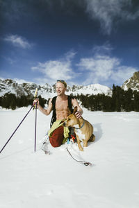 Cheerful hiker with dog on snowy field against mountains