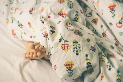 Low section of person lying under blanket on bed