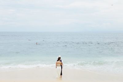 Rear view of couple standing at beach against sky