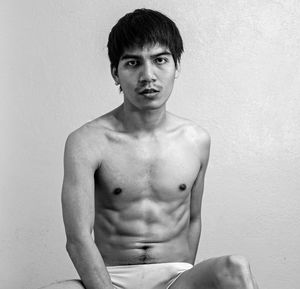 Portrait of shirtless man sitting against wall
