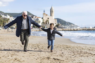 Happy senior man running with grandson at beach