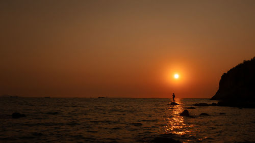 Silhouette fishing man standing on the rock inn the sea and the sunlight background at twilight 