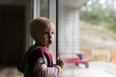 Girl with mouth open looking away while standing by window at home