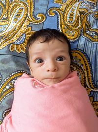 High angle portrait of cute baby boy wrapped in blanket lying on bed