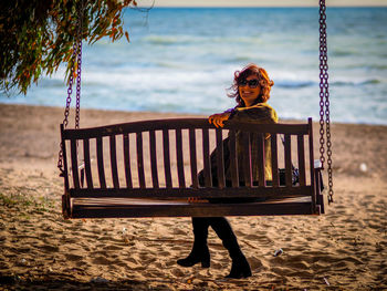 Smiling woman sitting on swing at beach