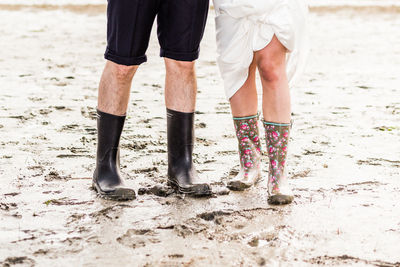 Low section of man and woman wearing rubber boots while standing mud