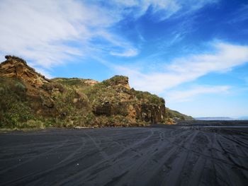 Black sand beach by rocky mountain against sky