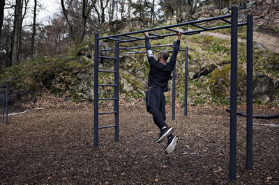 Full length rear view of man exercising on monkey bars at outdoor gym