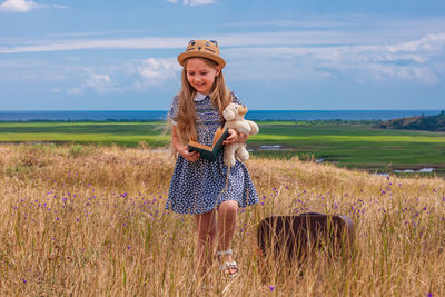 Child girl in straw hat and dress sitting on vintage suitcase reading book. cute kid with soft  toy 