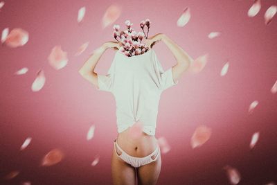 Young woman taking off t-shirt while standing against pink background