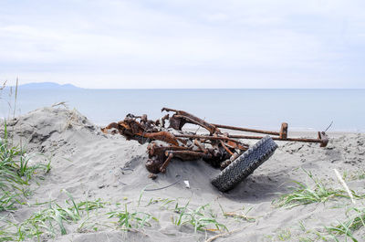 Rusty car wreck on sandbeach by sea against sky