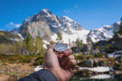 Cropped hand of man holding sunglasses against mountain