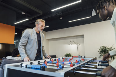 Mature businessman playing foosball with young colleague in office