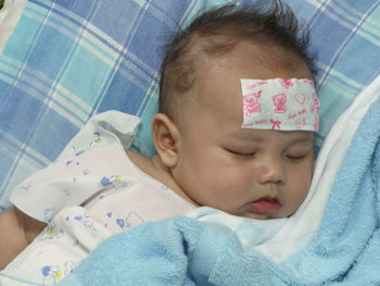 High angle view cute baby boy with bandage on forehead sleeping at home