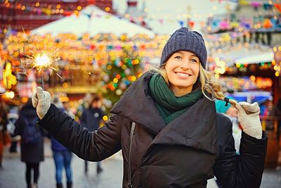 Portrait of smiling woman holding sparkler in market during winter