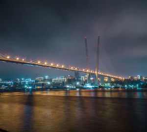 Illuminated bridge over river against sky at night