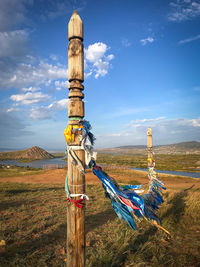 Cross on wooden post on field against sky