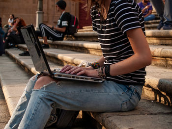 Midsection of woman using laptop while sitting on staircase