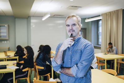 Portrait of confident male teacher with students studying in background