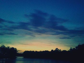 Silhouette trees against calm lake at sunset