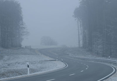 Snow covered road by trees against sky during winter