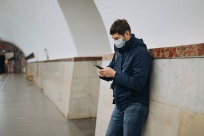 Man wearing mask using phone in corridor