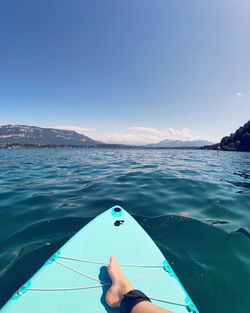 Low section of man sitting on surfboard in sea against sky